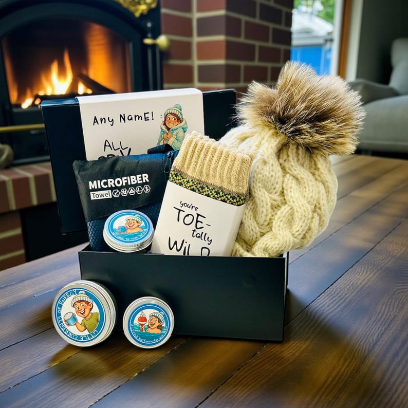Pu&ograve; includere: Una scatola regalo nera contenente un cappello a maglia a trecce color crema con un pompon in pelliccia marrone, calzini beige, un asciugamano in microfibra e piccole lattine. Il cappello e i calzini sono beige. La scatola ha il testo "Any Name!" e "ALL".