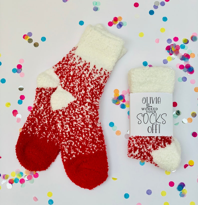 以下が含まれることがあります： 「Olivia You Worked Your Socks Off!」と書かれた白いタグが付いた、赤と白のふわふわしたソックスのペア