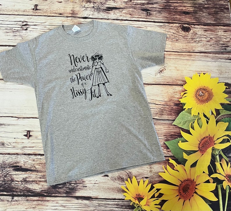 Puede incluir: Camiseta gris con un gr&aacute;fico negro de una mujer con el texto "Nunca subestimes el poder de un berrinche."