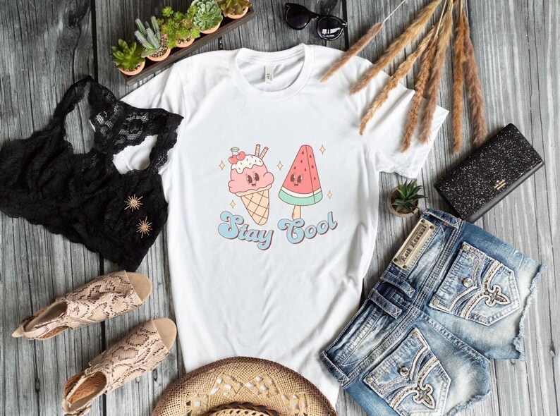 Puede incluir: Camiseta blanca con un gr&aacute;fico de un cono de helado y una paleta de sand&iacute;a con el texto "Stay Cool".