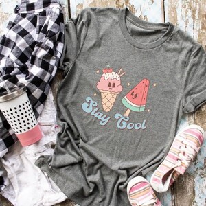 Puede incluir: Camiseta gris con un gr&aacute;fico de un cono de helado y una paleta de sand&iacute;a. El texto "Stay Cool" est&aacute; impreso debajo del gr&aacute;fico.