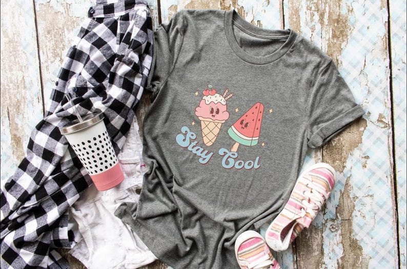 Puede incluir: Camiseta gris con un gr&aacute;fico de un cono de helado y una paleta de sand&iacute;a. El texto "Stay Cool" est&aacute; impreso debajo del gr&aacute;fico.