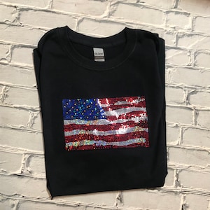 May include: A black t-shirt with a sequined American flag design. The flag is red, white, and blue with iridescent sequins.