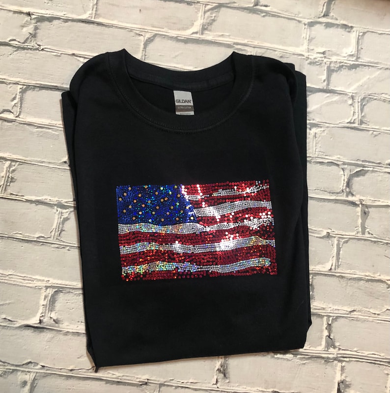 May include: A black t-shirt with a sequined American flag design. The flag is red, white, and blue with iridescent sequins.