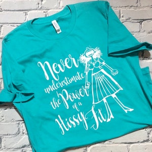Puede incluir: Una camiseta azul turquesa con un dise&ntilde;o gr&aacute;fico blanco. El gr&aacute;fico presenta a una mujer de dibujos animados con una expresi&oacute;n de sorpresa y el texto "Nunca subestimes el poder de un berrinche."