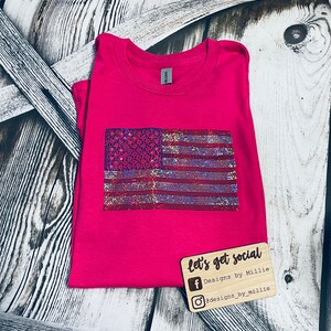 May include: A pink t-shirt with a sparkly American flag design. The shirt has the text "let's get social" and social media handles for Designs by Millie.