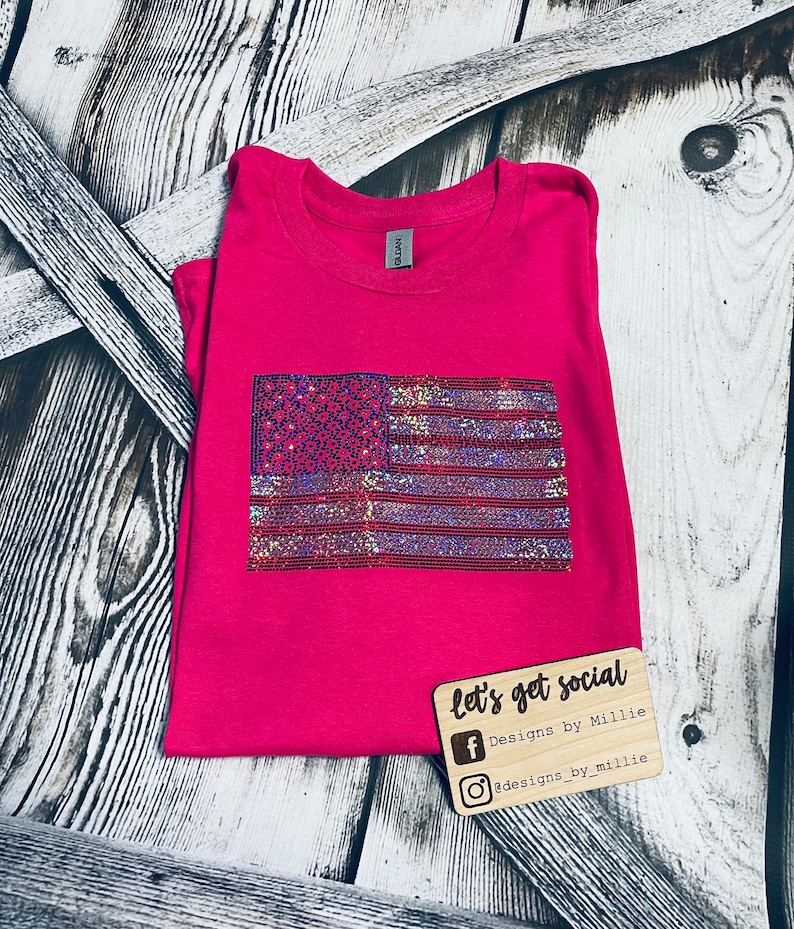 May include: A pink t-shirt with a sparkly American flag design. The shirt has the text "let's get social" and social media handles for Designs by Millie.