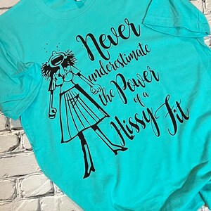 Puede incluir: Una camiseta turquesa con un gr&aacute;fico negro de una mujer con una expresi&oacute;n dram&aacute;tica y el texto "Nunca subestimes el poder de una rabieta."