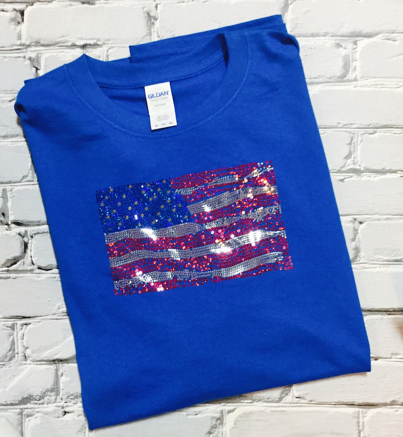 May include: A royal blue t-shirt with a sequined American flag design. The flag is made of red, white, and blue sequins.
