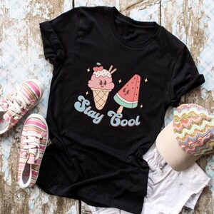 Puede incluir: Camiseta negra con un gr&aacute;fico de un cono de helado y una paleta de sand&iacute;a. El texto "Stay Cool" est&aacute; impreso en una fuente retro.