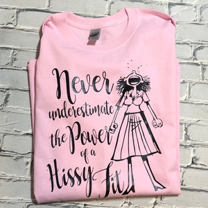 Puede incluir: Camiseta rosa con un gr&aacute;fico negro de una mujer con una expresi&oacute;n de sorpresa y el texto "Nunca subestimes el poder de un berrinche."