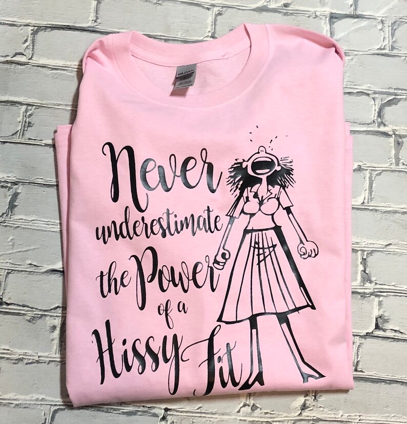 Puede incluir: Camiseta rosa con un gr&aacute;fico negro de una mujer con una expresi&oacute;n de sorpresa y el texto "Nunca subestimes el poder de un berrinche."