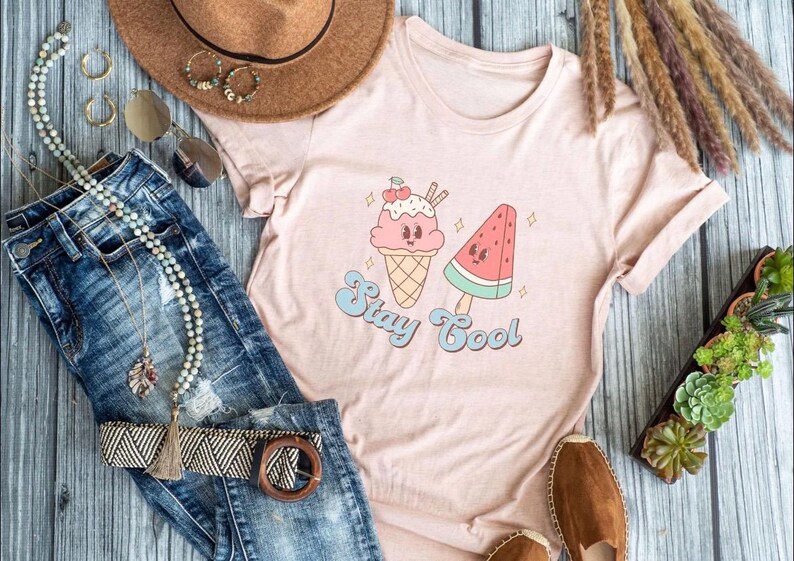 Puede incluir: Una camiseta rosa con un gr&aacute;fico de un cono de helado y una paleta de sand&iacute;a con el texto "Stay Cool".