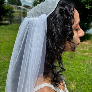 May include: A white bridal veil with a beaded crown. The veil is made of tulle and has a delicate, flowing design. The crown is adorned with small, sparkling beads.