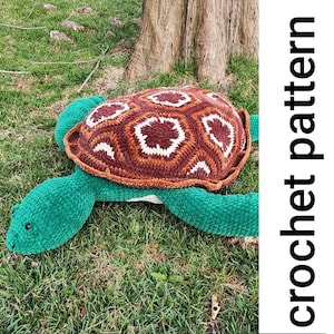 Puede incluir: Un juguete de tortuga de crochet con una concha marrón y blanca y un cuerpo verde. La tortuga está tumbada en la hierba verde.