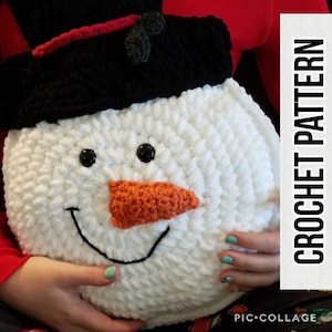 May include: A white crocheted snowman pillow with a black top hat, red trim, and a green holly berry. The snowman has black eyes, a black smile, and an orange carrot nose.