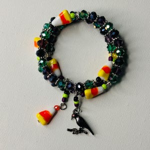 Könnte beinhalten: Ein Halloween-Armband mit Süßmais-Anhängern, schwarzen und grünen Kristallperlen und einem schwarzen Raben-Anhänger.