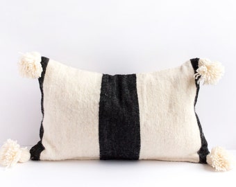 May include: A white and black striped throw pillow with white pom-poms on the corners.