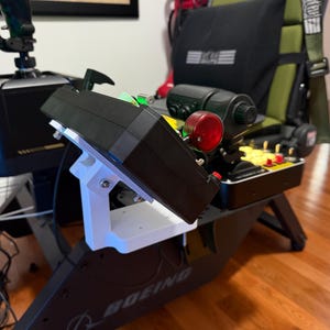 Op de afbeelding: Een vluchtsimulator cockpitopstelling met een zwart bedieningspaneel gemonteerd op een witte 3D-geprinte beugel. De console bevat een opvallende rode ronde schakelaar, diverse gele knoppen en een zwarte gashendel op een Boeing-basis.