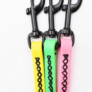 Puede incluir: Tres correas para perros con cierres negros y costuras negras. Las correas son amarillas, verdes y rosas.