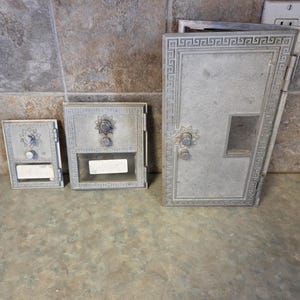May include: Three antique silver mailboxes of varying sizes are displayed. The largest mailbox has a door with a decorative border and a small window. The smaller mailboxes have a similar design with a knob and a slot for mail. The mailboxes are made of metal.
