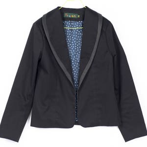 Pode incluir: Um blazer preto com uma gola larga e um forro de bolinhas azuis e brancas. O blazer tem um fecho de correr e &eacute; feito de um tecido macio e confort&aacute;vel.