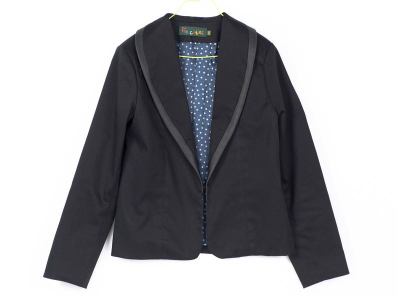 Pode incluir: Um blazer preto com uma gola larga e um forro de bolinhas azuis e brancas. O blazer tem um fecho de correr e &eacute; feito de um tecido macio e confort&aacute;vel.