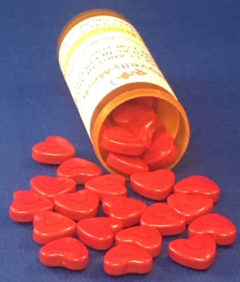May include: A clear plastic bottle with a white label that reads "Love is..." and a red heart design. The bottle is tipped over, spilling out red heart-shaped pills.