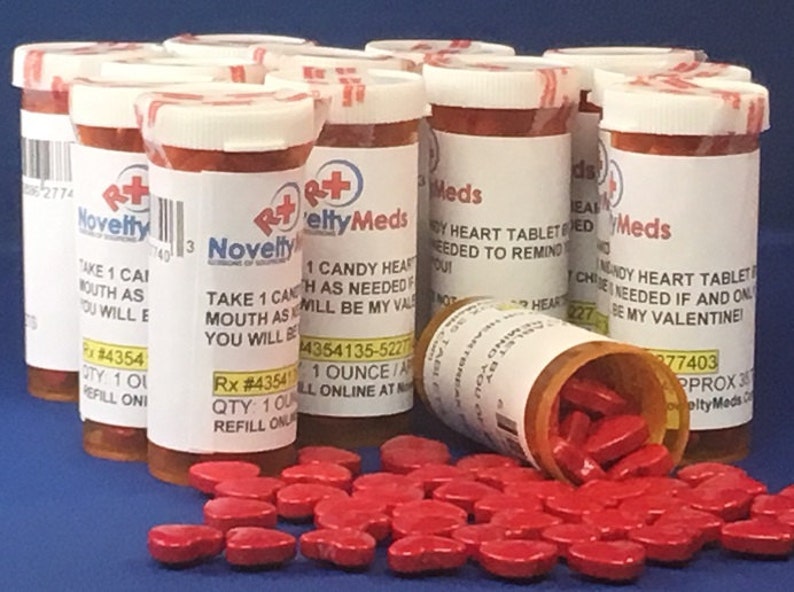 May include: Multiple red plastic pill bottles with white lids and labels that say "NoveltyMeds" and "1 Candy Heart Tablet Each As Needed If And Only If You Will Be My Valentine!"  The bottles are filled with red heart-shaped candy.