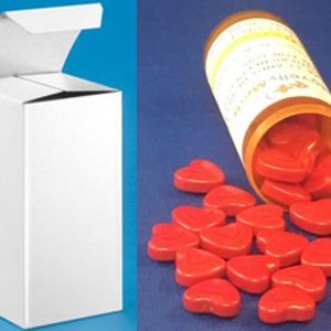 May include: A white cardboard box with a hinged lid, partially open, next to a clear glass bottle with a red label. The bottle is tipped over, spilling out red heart-shaped pills.