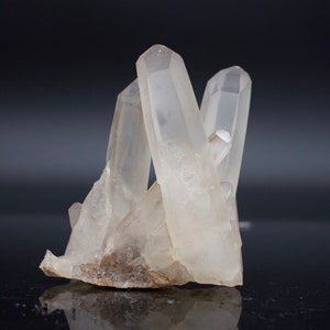 Puede incluir: Un grupo de cristales de cuarzo transparentes con una base rugosa y natural. Los cristales son puntiagudos y translúcidos, con un ligero tono lechoso.