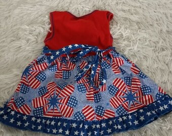 May include: A red, white, and blue sleeveless dress with a star print and a ruffled hem. The dress has a tie at the waist.