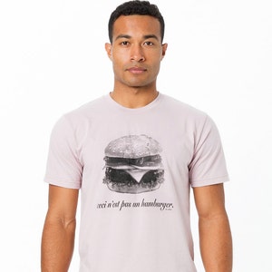 May include: A light pink t-shirt with a black and white image of a hamburger and the text "ceci n'est pas un hamburger".