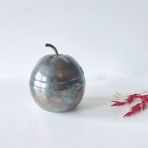 Może przedstawiać: Srebrna cukiernica w kształcie jabłka z pokrywką. Cukiernica ma lekko matowe wykończenie, co nadaje jej vintage'owy wygląd.