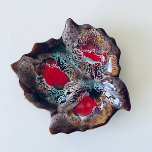 Puede incluir: Un plato de cerámica con forma de hoja con un esmalte marrón, rojo y blanco. El plato tiene un borde ondulado y un interior profundo y redondeado.