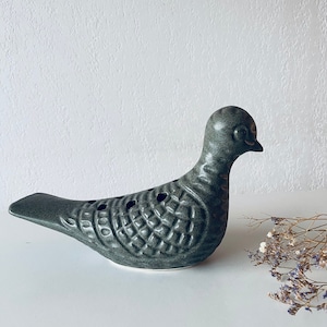 以下が含まれることがあります： テクスチャ加工された表面を持つ濃い緑色のセラミック製の鳩の置物。鳩は小さなくちばしを持っており、白い表面の上に置かれています。