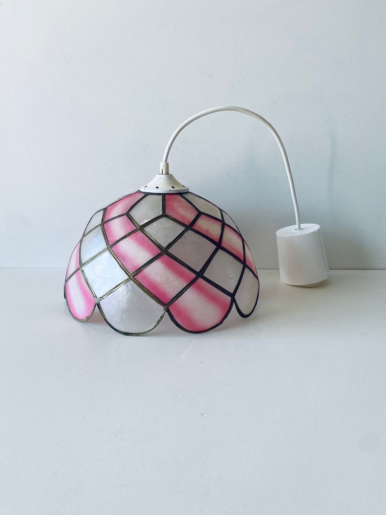 Puede incluir: Una l&aacute;mpara colgante blanca con una pantalla de vidrio tintado rosa y blanco. La pantalla tiene un patr&oacute;n geom&eacute;trico y un borde festoneado.