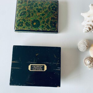 K&ouml;nnte beinhalten: Eine schwarze Box mit einem gr&uuml;nen und goldenen Blumendesign auf der Oberseite. Die Unterseite der Box tr&auml;gt ein Etikett mit der Aufschrift "Shikara, Vases de l'Inde, 40 rue du Faubourg St. Denis, 75010 Paris".