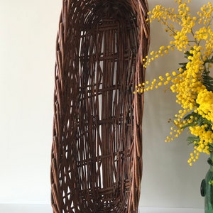 Puede incluir: Una cesta de mimbre grande, de forma ovalada, hecha de mimbre marr&oacute;n tejido. La cesta est&aacute; vac&iacute;a y tiene un acabado liso y natural.