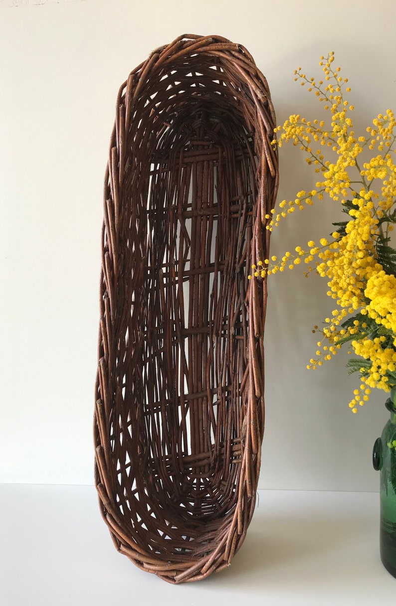 Puede incluir: Una cesta de mimbre grande, de forma ovalada, hecha de mimbre marr&oacute;n tejido. La cesta est&aacute; vac&iacute;a y tiene un acabado liso y natural.