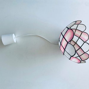 Puede incluir: Una l&aacute;mpara colgante de vidrio coloreado blanco y rosa con un borde festoneado.