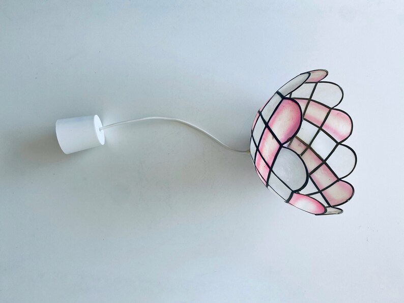 Puede incluir: Una l&aacute;mpara colgante de vidrio coloreado blanco y rosa con un borde festoneado.