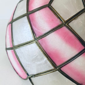 Puede incluir: Una pantalla de l&aacute;mpara de vidrio coloreado rosa y blanco con un patr&oacute;n geom&eacute;trico. La pantalla est&aacute; hecha de paneles de vidrio que se mantienen unidos por un marco de metal.