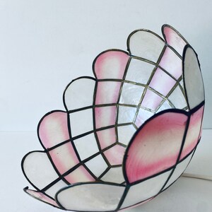 Puede incluir: Una pantalla de l&aacute;mpara blanca y rosa con un patr&oacute;n geom&eacute;trico. La pantalla est&aacute; hecha de un material delgado y transl&uacute;cido y tiene un borde festoneado.