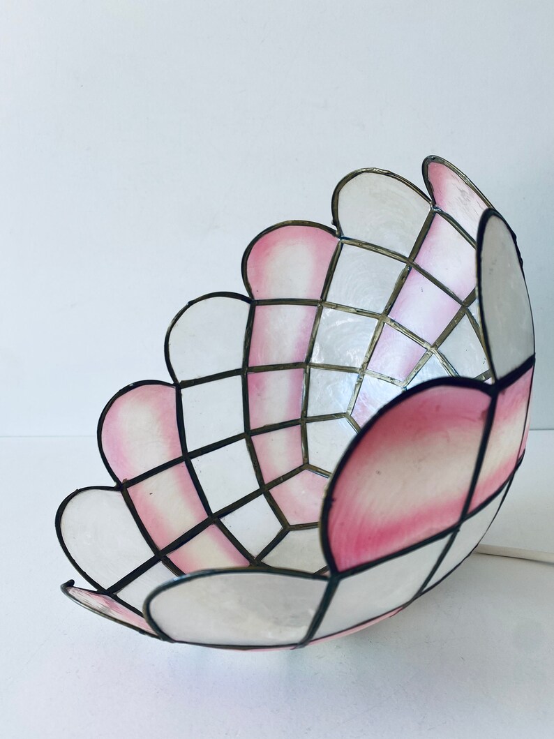 Puede incluir: Una pantalla de l&aacute;mpara blanca y rosa con un patr&oacute;n geom&eacute;trico. La pantalla est&aacute; hecha de un material delgado y transl&uacute;cido y tiene un borde festoneado.