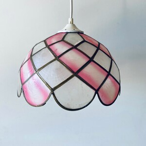 Puede incluir: Una l&aacute;mpara colgante de cristal de colores rosa y blanco con un borde festoneado. La luz cuelga de un cable blanco.