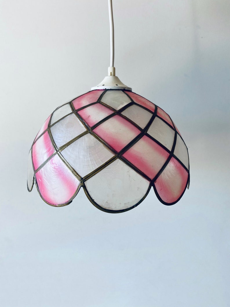 Puede incluir: Una l&aacute;mpara colgante de cristal de colores rosa y blanco con un borde festoneado. La luz cuelga de un cable blanco.