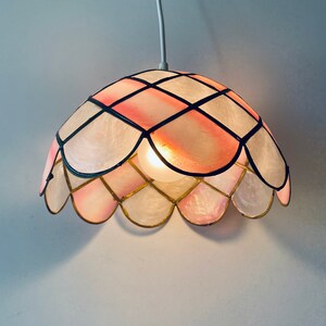 Puede incluir: Una l&aacute;mpara colgante de cristal de colores rosa y blanco con un borde festoneado. La luz cuelga de un cable blanco.