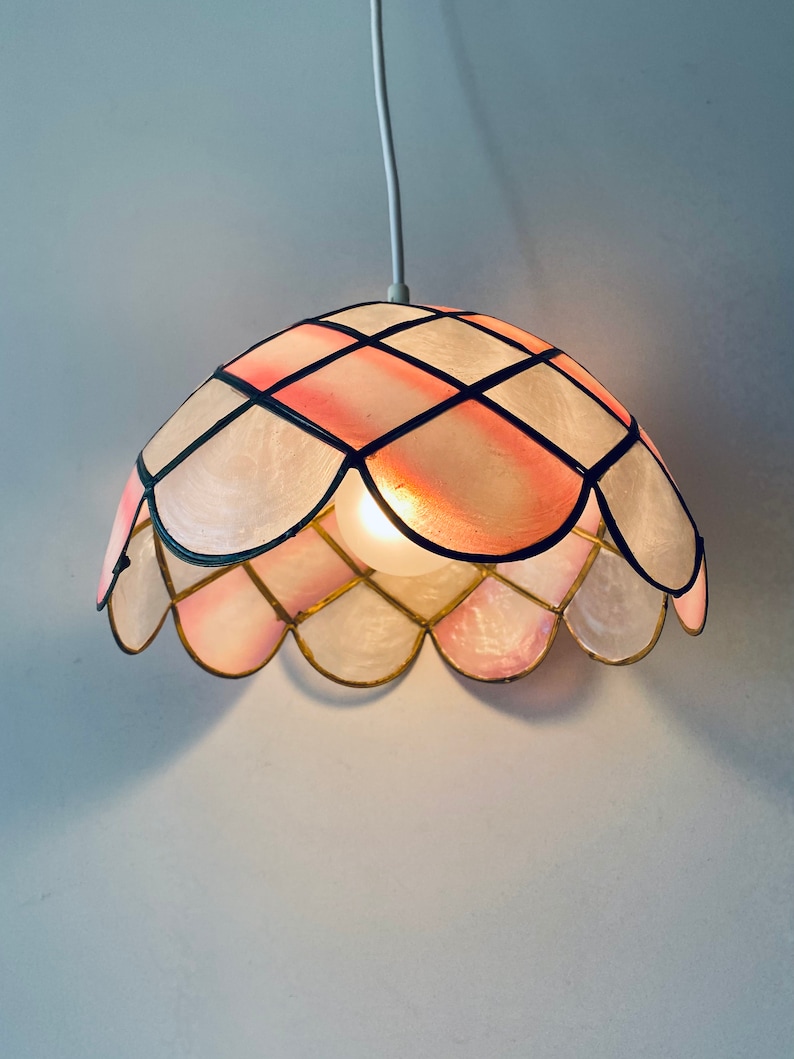 Puede incluir: Una l&aacute;mpara colgante de cristal de colores rosa y blanco con un borde festoneado. La luz cuelga de un cable blanco.