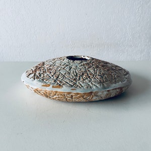 Peut inclure: Un vase en céramique blanche avec un motif texturé brun. Le vase a la forme d'un bol peu profond avec une large ouverture.